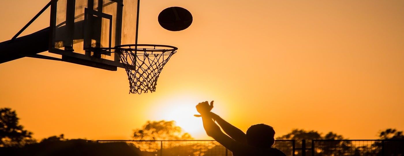 Homem arremessando bola de basquete na cesta ao por do sol